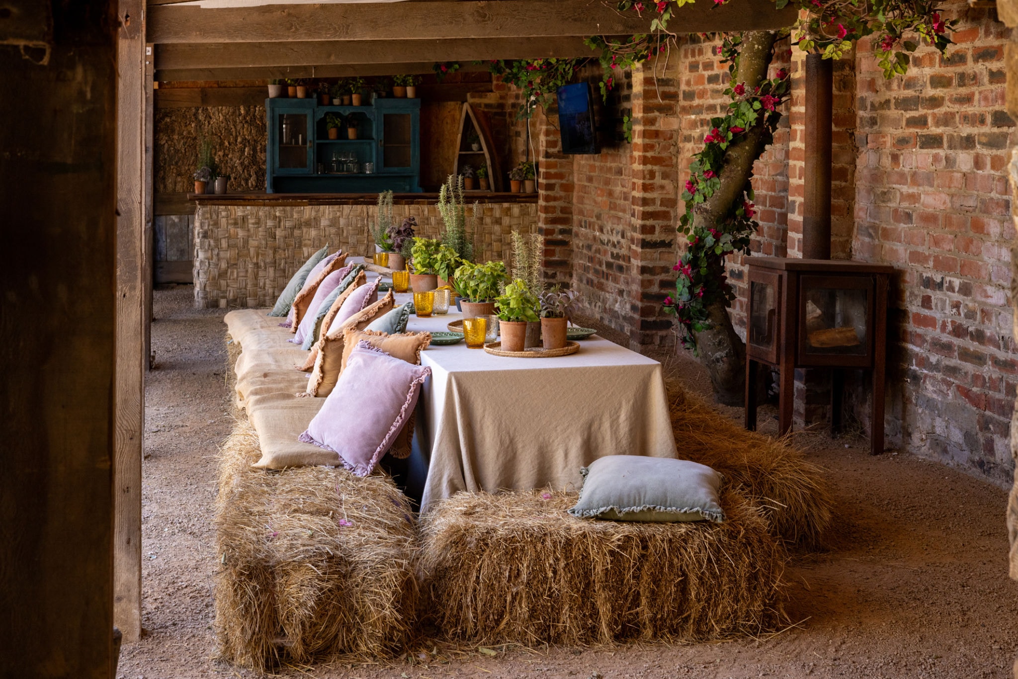 Rustic barn table set with hay bales, pillows, and potted plants — a warm gathering space